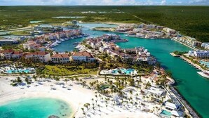 An aerial view of a resort with multiple buildings, a marina, and a beach with sun loungers. - Stylish Cap Cana Apartment • Pool, Gym & Beaches (Punta Cana)