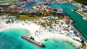 An aerial view of a coastal resort with multiple buildings, a marina, and a beach. - Resort-Style Golf & Ocean view  Cap Cana (Punta Cana)