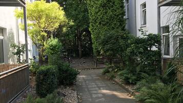 A narrow pathway flanked by dense greenery and buildings with balconies.