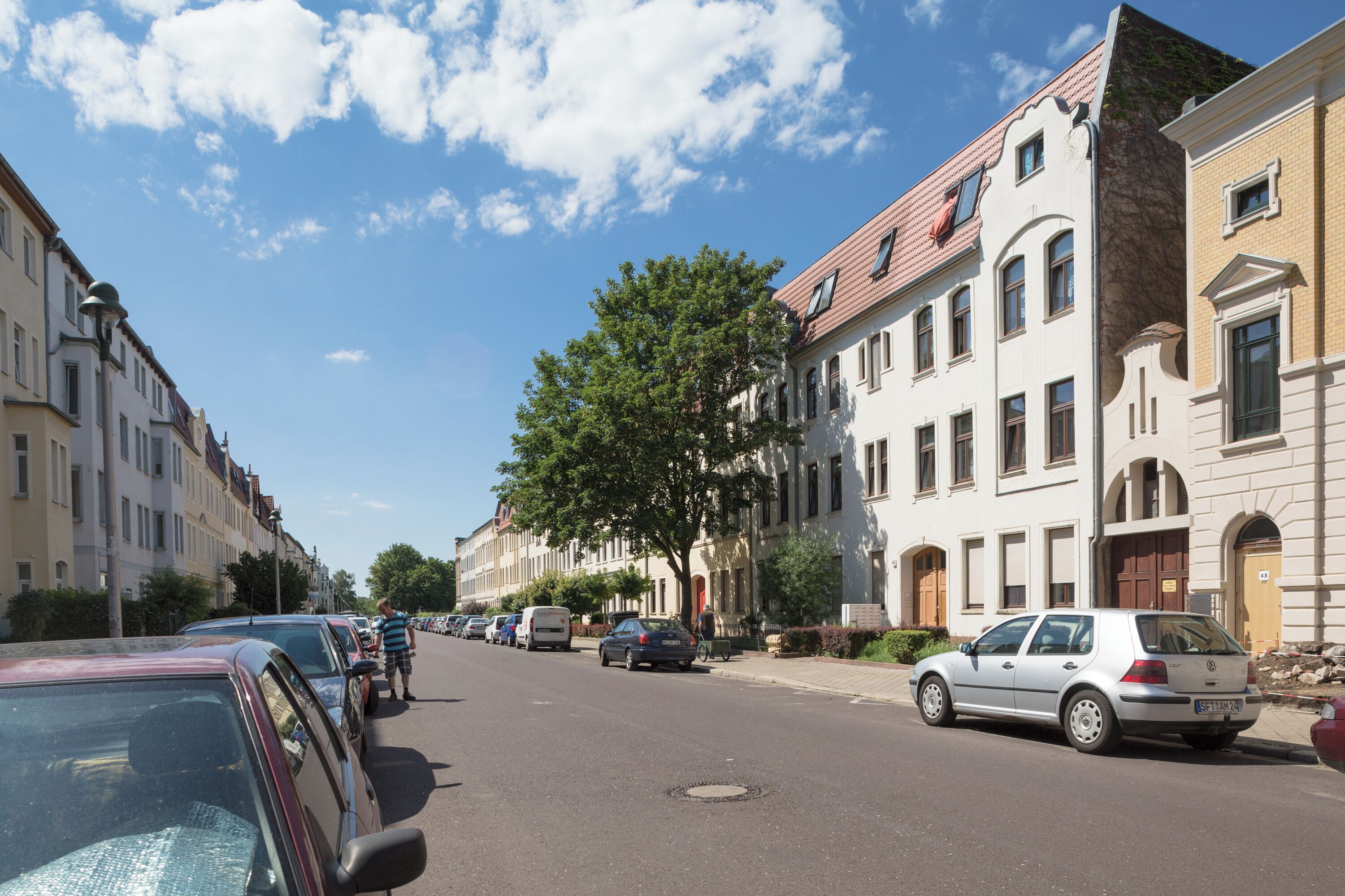 A street lined with historic buildings, parked cars, and a clear sky.