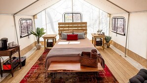 Una habitación con tienda de campaña, una cama, mesitas de noche, un tapete rojo y una silla negra.