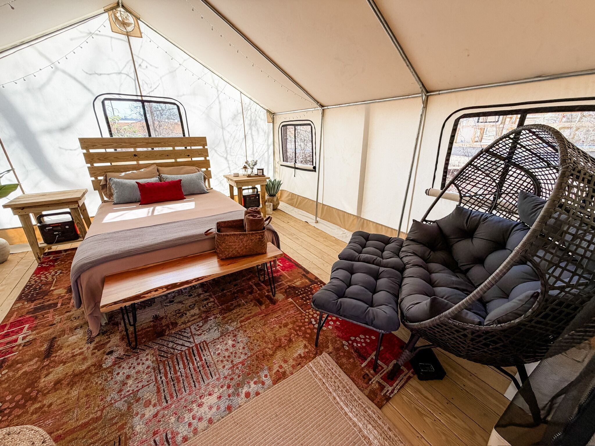 A tented accommodation with a bed, a hanging chair, and a small table with a radio.