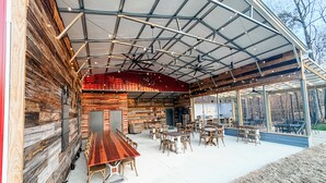 Un edificio de madera rústico con un porche cubierto que tiene mesas y sillas, una gran mesa de madera y vistas al exterior.
