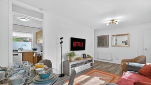 Ein modernes Wohnzimmer mit Essbereich, einer Küche im Hintergrund, einem Flachbildfernseher und einem großen Spiegel.