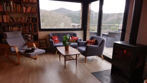 Un salon chaleureux avec une cheminée, une bibliothèque, un canapé et une vue sur l’extérieur.