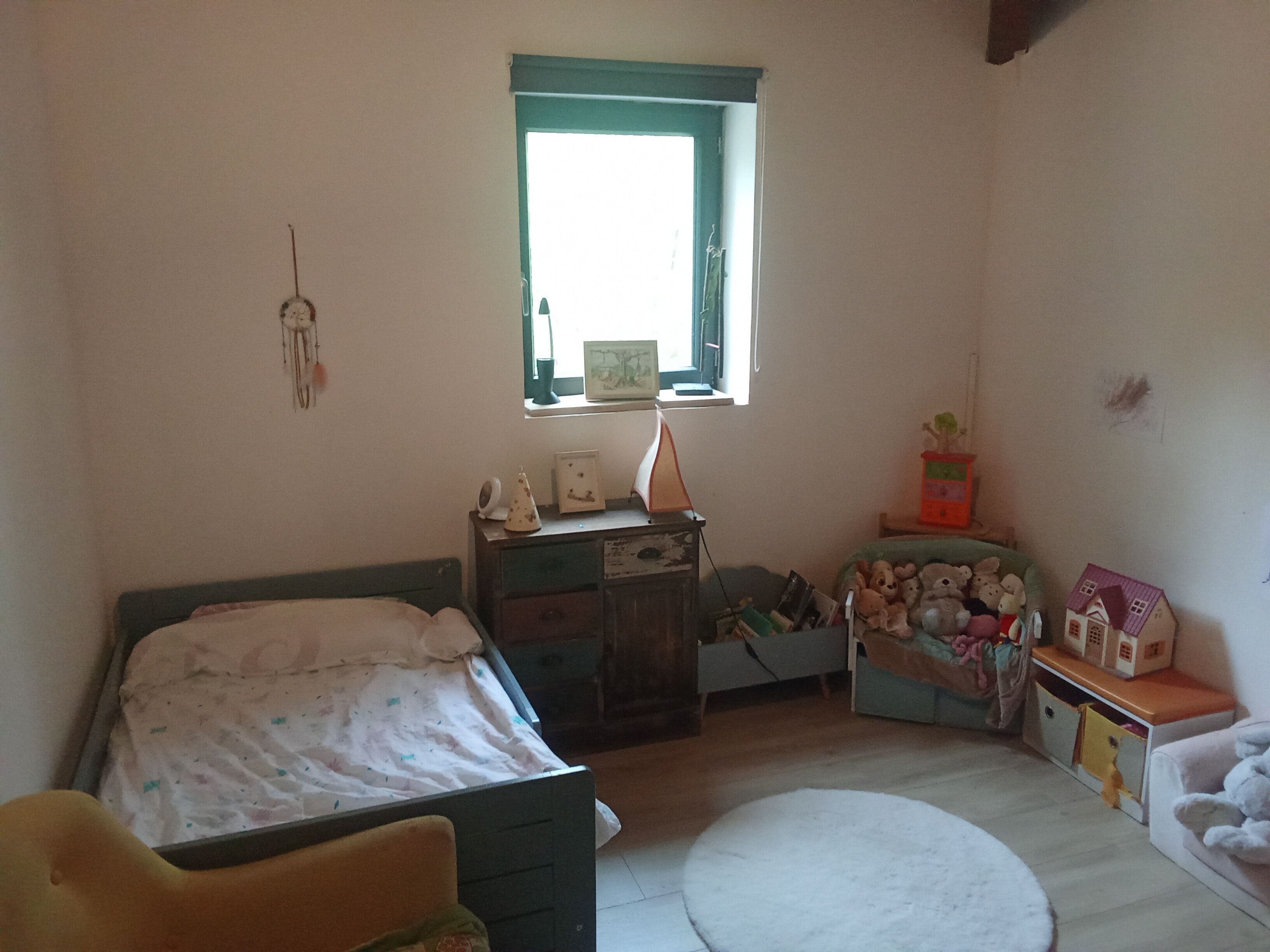 A bedroom with a bed, dresser, window, and a small table with toys.