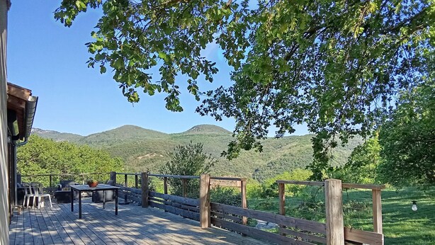 Une terrasse en bois avec des meubles d’extérieur, une clôture en bois et une vue sur des collines verdoyantes.