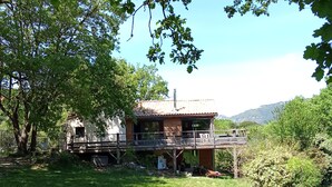 Un chalet rustique doté d’un balcon, entouré d’une végétation luxuriante et avec des montagnes en toile de fond.