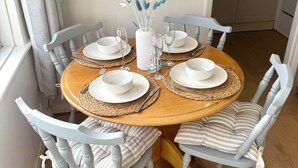 A dining table set with white plates, glasses, and a vase with blue and white flowers. - Cornish coastal escape, close to the beach, shops, cafes and restaurants. (Bude)