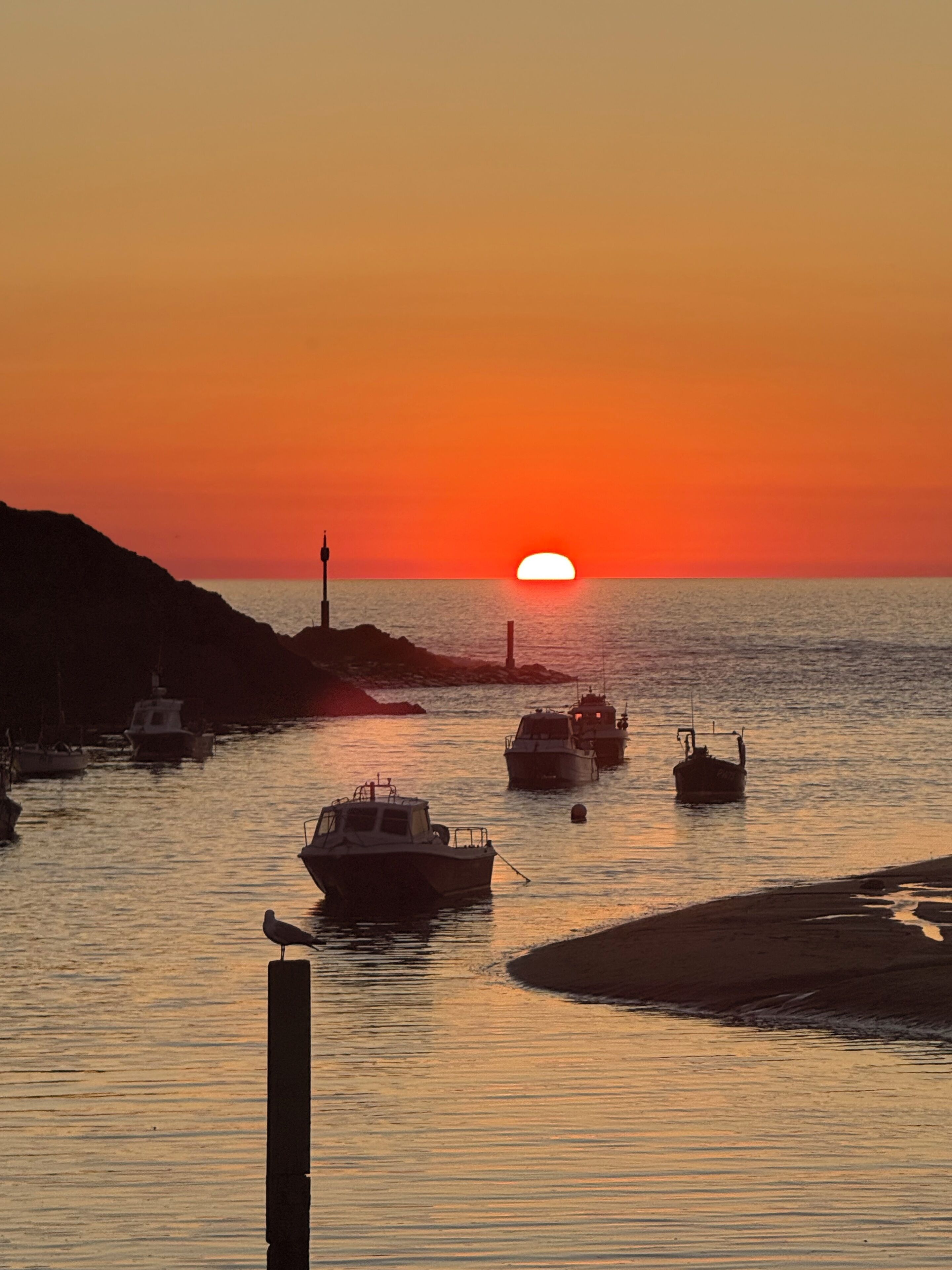 Een zonsondergang boven een kalme zee, met boten afgemeerd langs de kust.