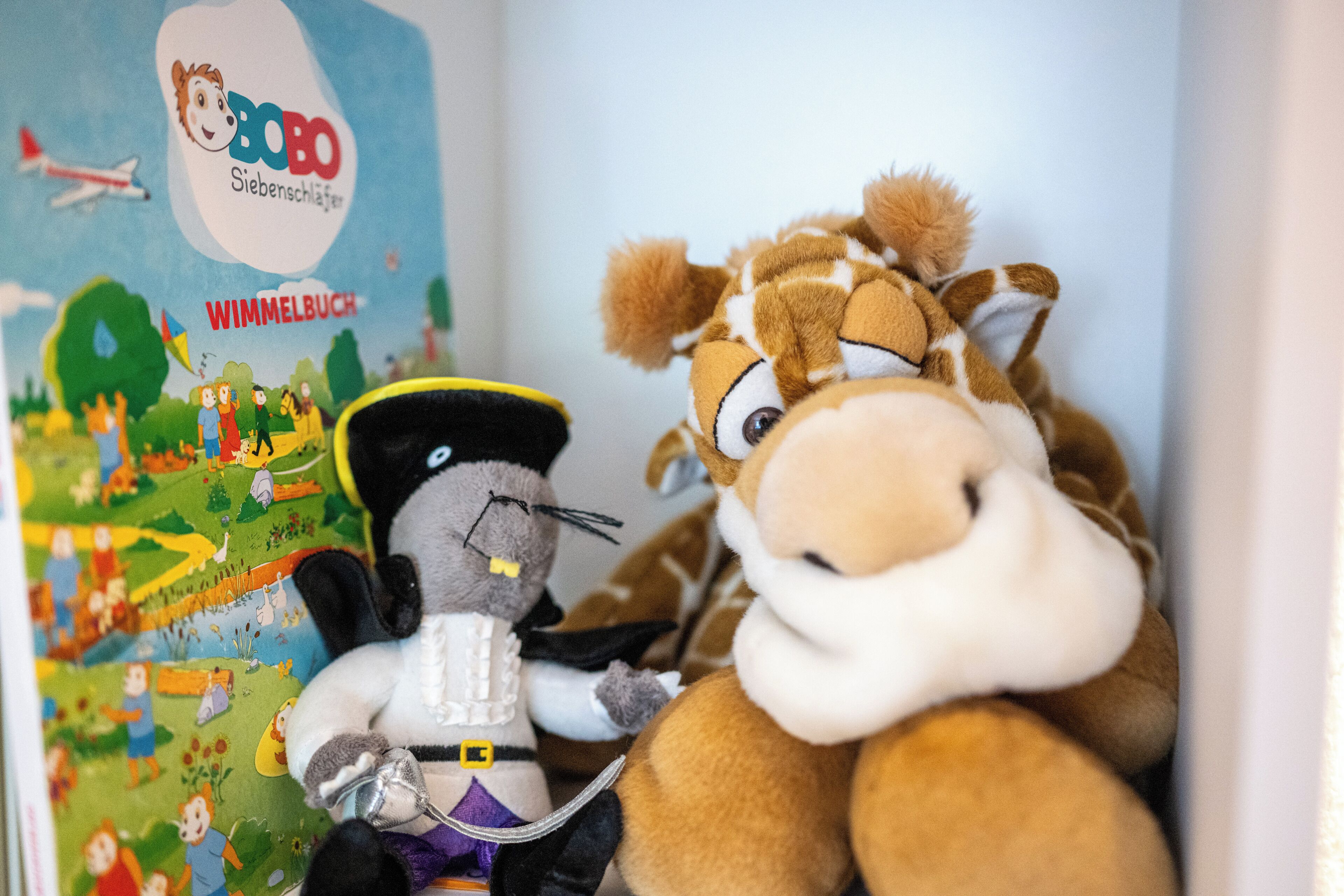 A plush toy giraffe and a plush toy cat in a room with a colorful wall mural.