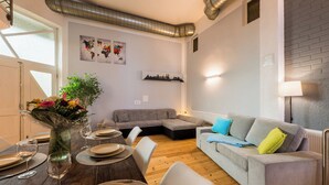 A modern living room with a dining area, a grey sofa with colorful cushions, a wooden dining table set for a meal, and artwork on the walls. - Spacious ground floor loft with 140 m² - ideal for families & groups of up to 6 (7) people (Magdeburg)