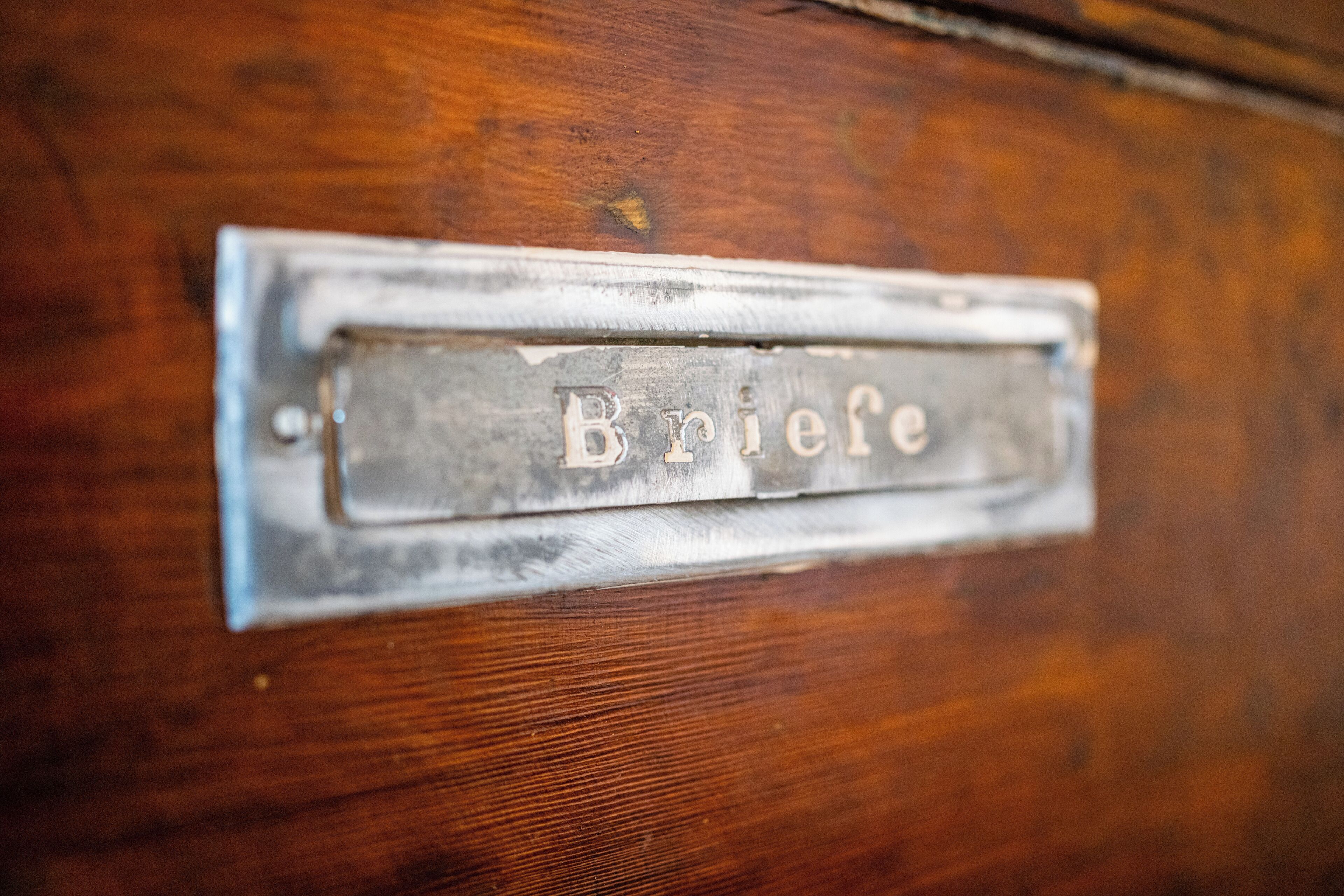 Een metalen naambordje met de tekst 'Briefe' op een houten ondergrond.