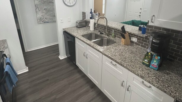 Una cocina moderna con armarios blancos, encimeras de granito, un lavabo doble y un reloj en la pared.