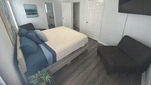 Un dormitorio con una cama, televisión, ventilador de techo y una puerta que da a otra habitación.