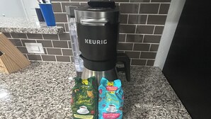 Una cocina con una cafetera Keurig, un paquete de café brasileño Great Gend, de familia, y un paquete de café Donut Shop Blend.