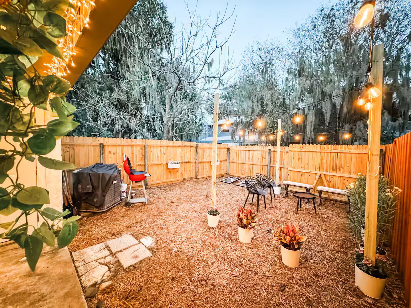 A backyard with a wooden fence, outdoor seating, and string lights.