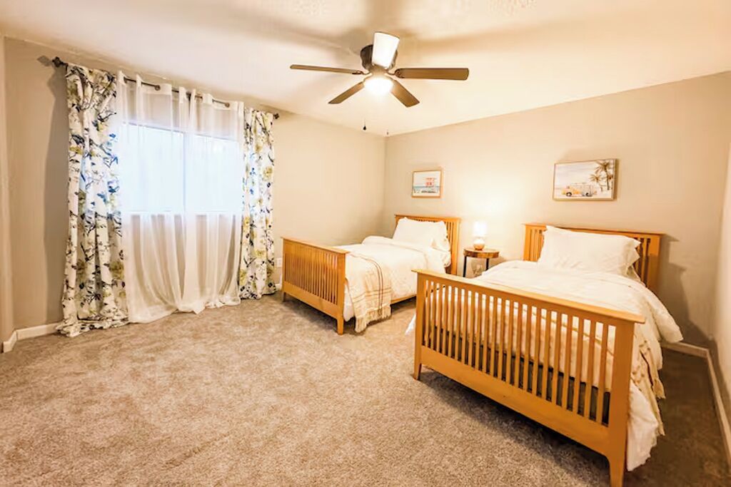 A bedroom with two wooden beds, a ceiling fan, and a window with floral curtains.