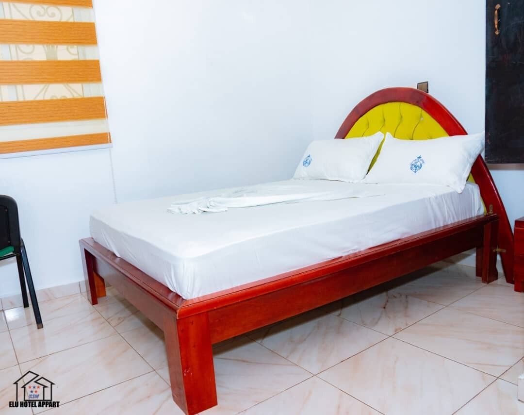 Een enkel bed met een houten frame en een hoofdbord met een geel kussen.