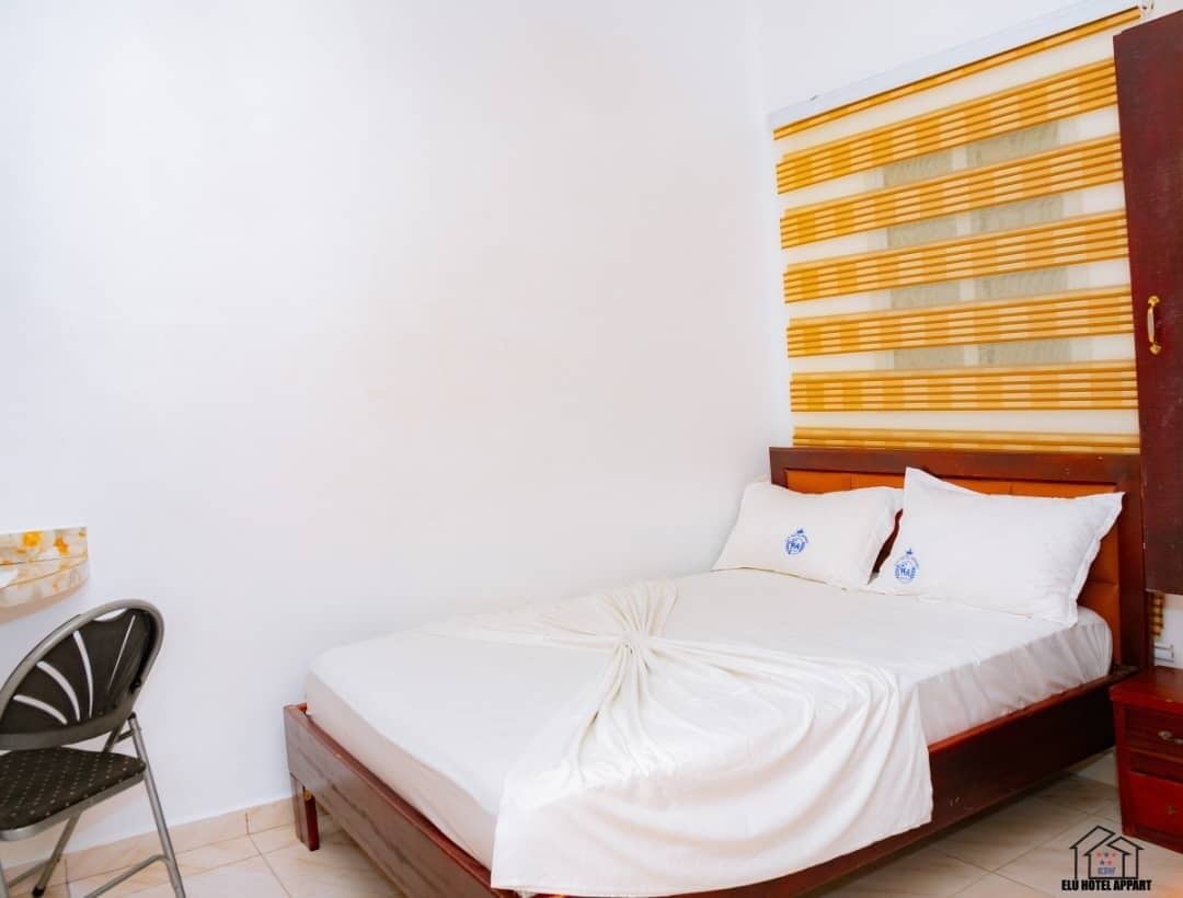 A bedroom with a wooden bed, white bedding, and a chair.