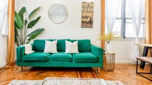 Un salon avec un canapé vert, un miroir rond, une affiche représentant New York et une plante.