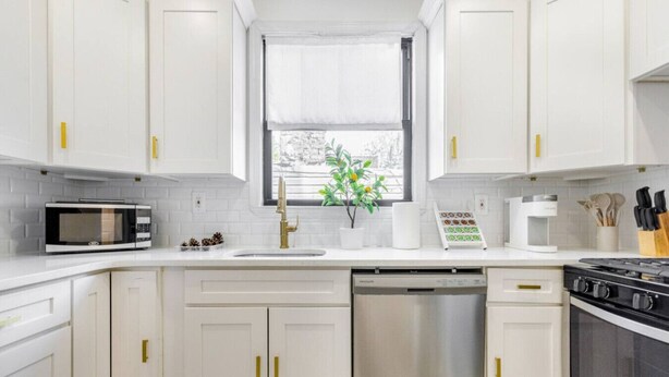Une cuisine moderne avec des meubles blancs, un lave-vaisselle en acier inoxydable, un four à micro-ondes, une machine à café et une cuisinière.