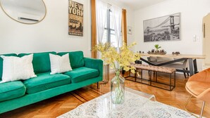 Un salon avec un canapé vert, une table basse surmontée d’un vase, un coin repas avec une table et des chaises, et un grand tableau encadré accroché au mur.