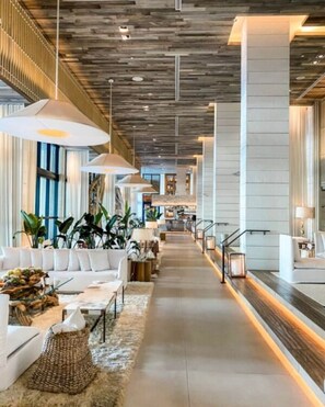 A spacious lobby with a central staircase, modern lighting, and a mix of seating areas. - Stunning Beach Condo with Balcony (Miami Beach)