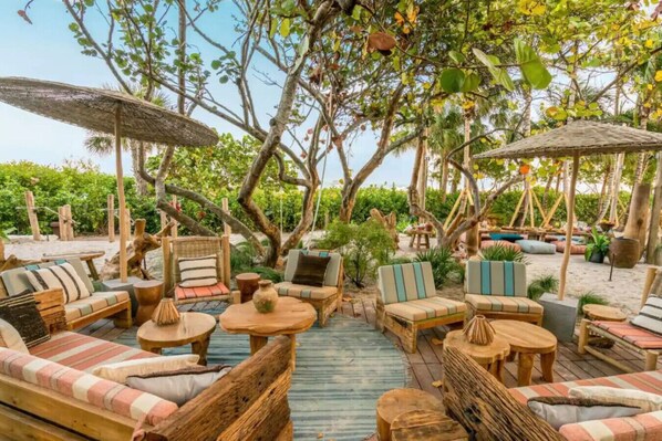 An outdoor seating area with wooden furniture and umbrellas, surrounded by lush greenery. - Stunning Beach Condo with Balcony (Miami Beach)