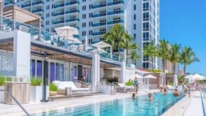 Un espace piscine aménagé avec des chaises longues et des parasols, entouré de grands immeubles.