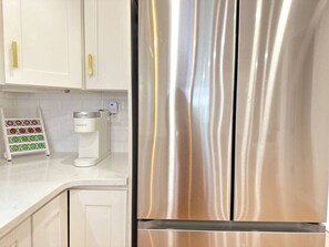 Un refrigerador de acero inoxidable en una cocina con armarios blancos y una cafetera sobre la encimera.