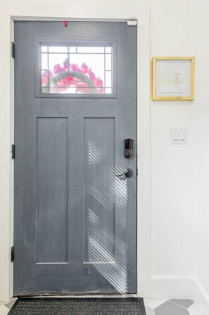 A grey door with a window, a doormat, and a framed quote on the wall.