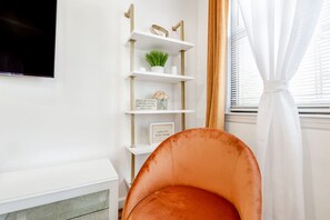 A living room with a white fireplace, a white shelving unit with decorative items, and a large window with curtains.