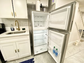 A kitchen with white cabinets, a stainless steel sink, and a refrigerator with open doors.