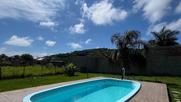 A rectangular swimming pool with a tiled deck, surrounded by a grassy area and a low wall. - Cantinho das Emerências, a house near the beach in a rustic style with a swimming pool! (Armação dos Búzios)