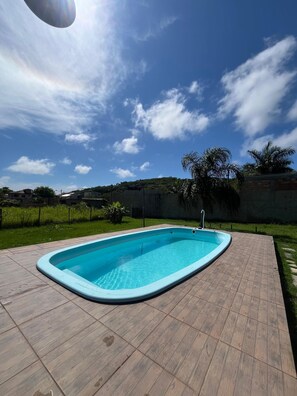 Une piscine rectangulaire, bordée d’une terrasse carrelée, entourée d’une pelouse et d’un petit muret.