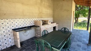 An outdoor patio with a brick oven, a table, and chairs. - Cantinho das Emerências, a house near the beach in a rustic style with a swimming pool! (Armação dos Búzios)