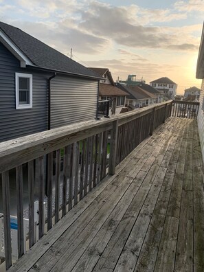 Une terrasse en bois dotée d’une rambarde, qui offre une vue sur un quartier résidentiel avec des maisons et un ciel dégagé.