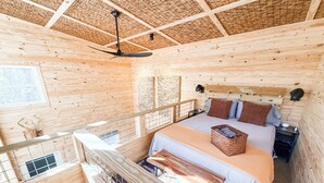 Een slaapkamer in een houten chalet met een bed, een plafondventilator, een raam en een balkon.