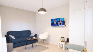 A modern living room with a blue sofa, a white chair, a small table, and a TV displaying a news program.