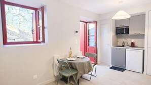 A compact kitchen with a microwave, sink, and small refrigerator. There is a dining area with a table and chairs, and a window with a view of trees.