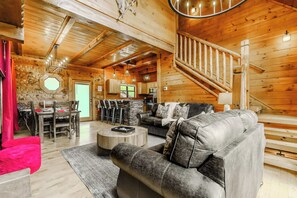 A log cabin interior with a dining area, a living room with a sofa and coffee table, and a staircase. - Dollywood & Pigeon Forge | Pool access | Sleeps 12 (Pigeon Forge)