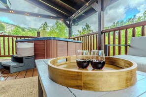 A wooden deck with a hot tub, a wooden table with a tray holding glasses of red wine, and a step stool. - Dollywood & Pigeon Forge | Pool access | Sleeps 12 (Pigeon Forge)