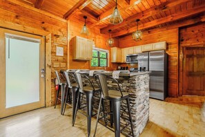 A wooden interior with a kitchen area, bar stools, and a refrigerator. - Dollywood & Pigeon Forge | Game room | Sleeps 12 (Pigeon Forge)