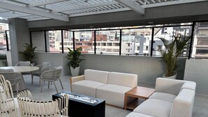 Eine moderne Dachterrassen-Lounge mit einer Couch, Sesseln, einem Tisch und Topfpflanzen.