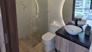 Ein modernes Badezimmer mit einer gläsernen Duschkabine, einer weißen Toilette und einer schwarzen Ablagefläche mit Waschtischbecken.