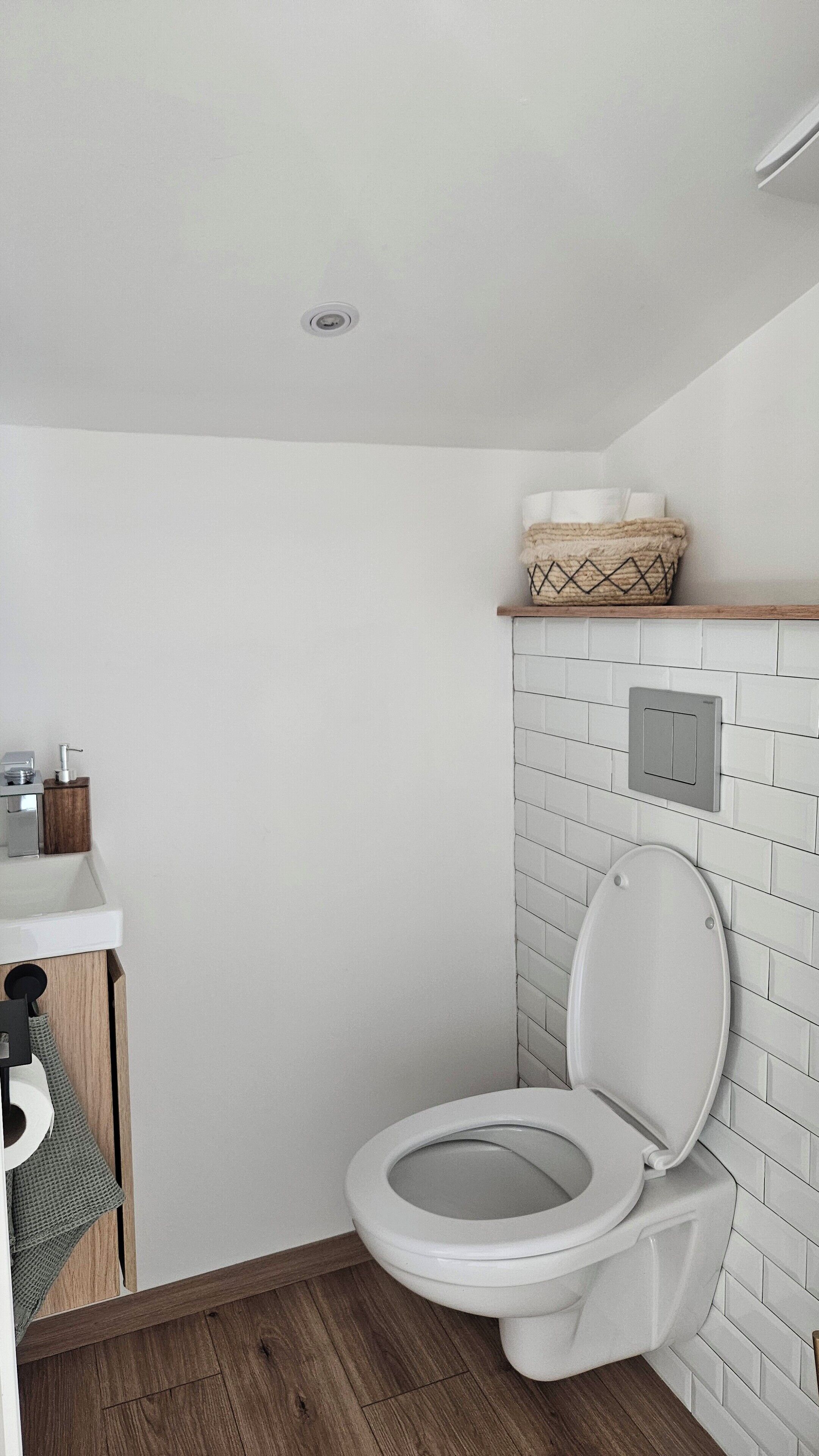 Ein kleines, modernes Badezimmer mit Toilette, Ablage für Toilettenartikel und einer weißen Fliesenwand.
