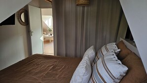 A bedroom with a bed, pillows, a hanging light, a door, and a view of an outdoor area. - Charming cocoon in the heart of the spa district (Vittel)