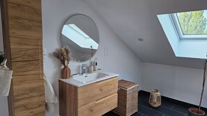 A modern bathroom with a wooden vanity, a round mirror, and a skylight. - Charming cocoon in the heart of the spa district (Vittel)
