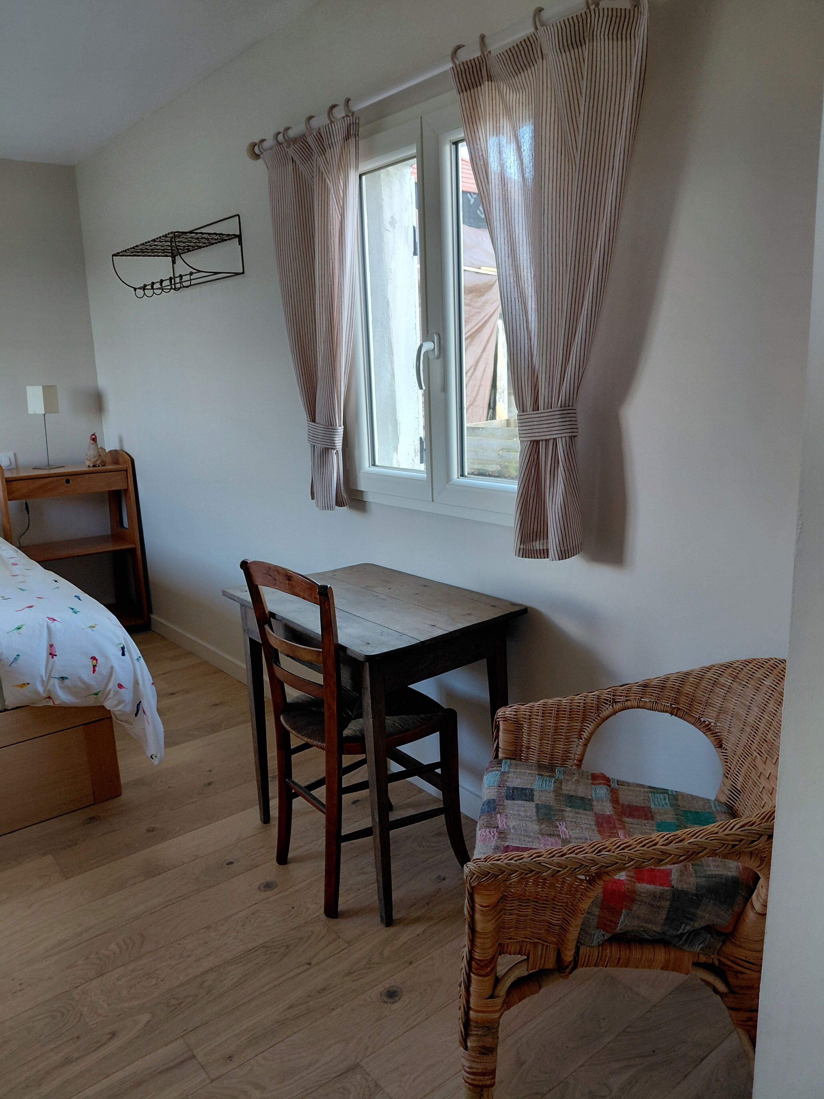 Un dormitorio con una cama de madera, un escritorio, una silla y un sillón de mimbre.